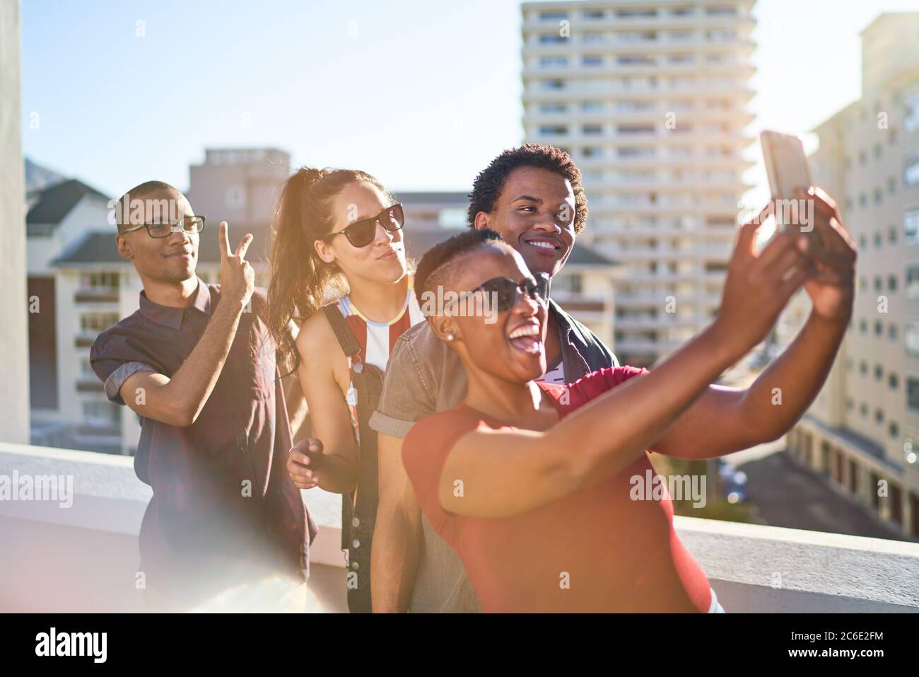 Young friends using smart phone on sunny urban rooftop balcony Stock Photo