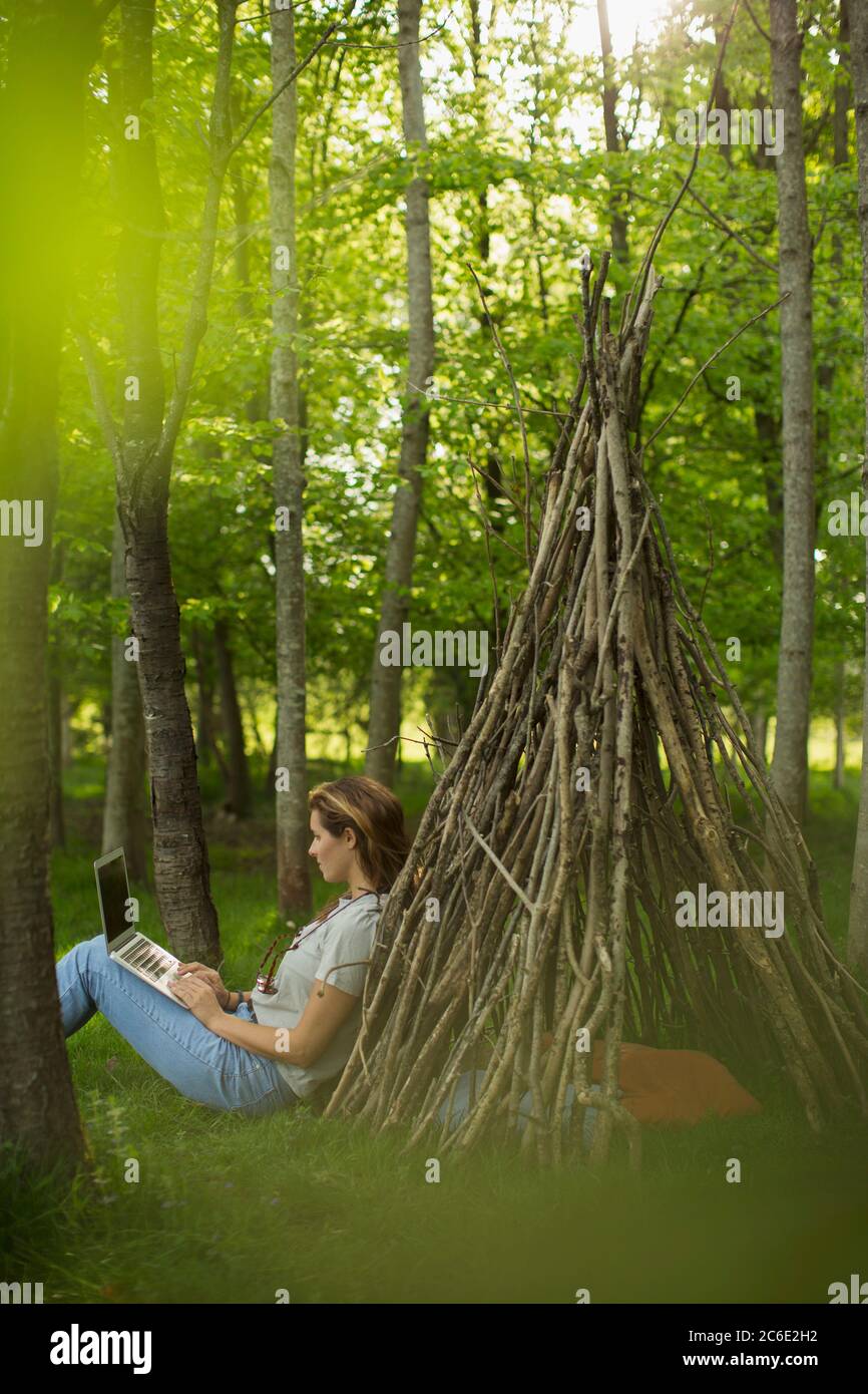 Woman using laptop at branch teepee in woodland Stock Photo