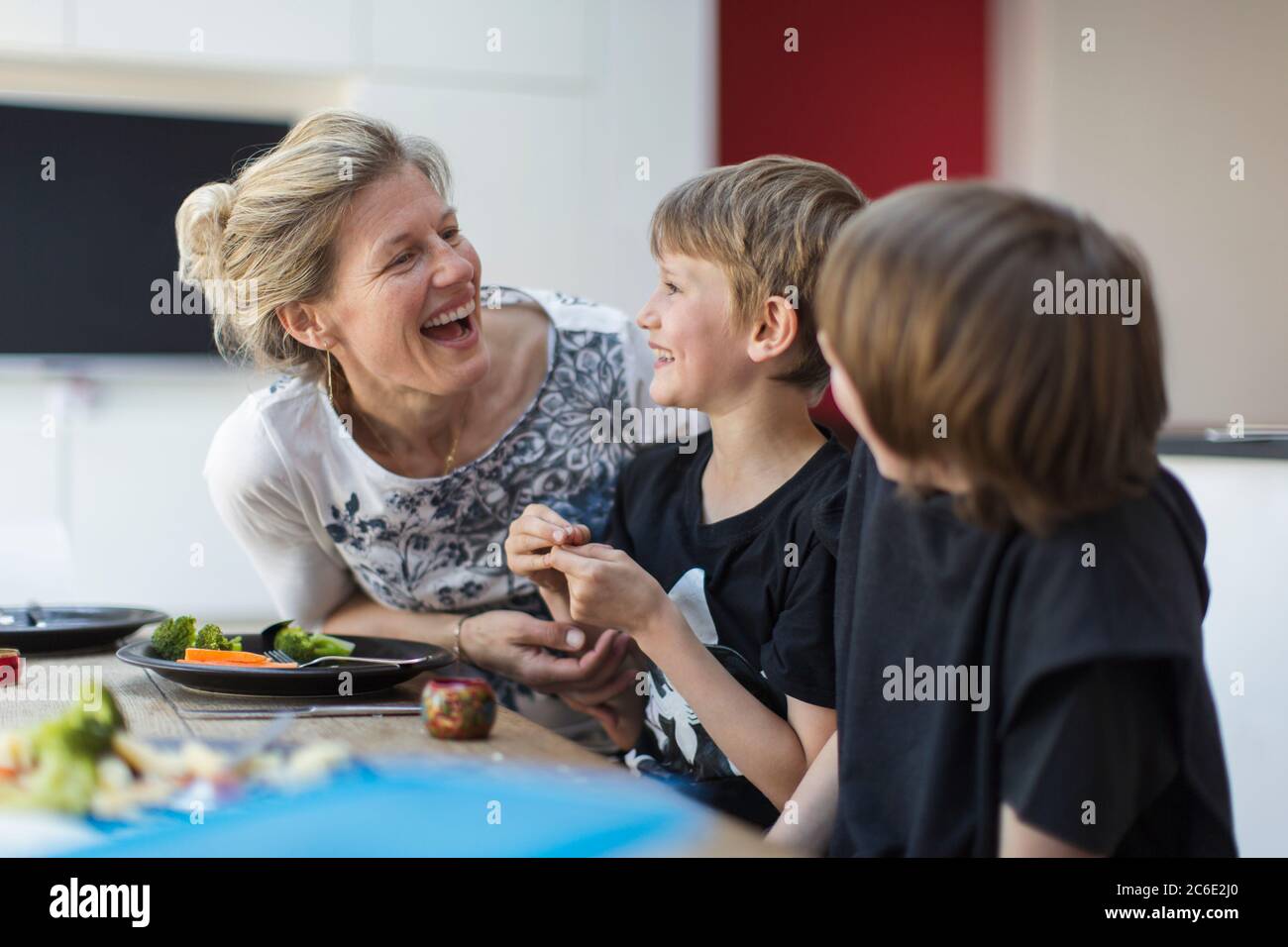 Happy mother and sons eating dinner at table Stock Photo