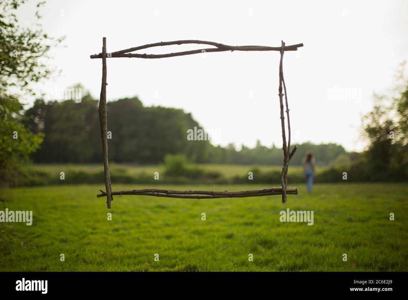 Branch frame over woman walking in idyllic grass field Stock Photo
