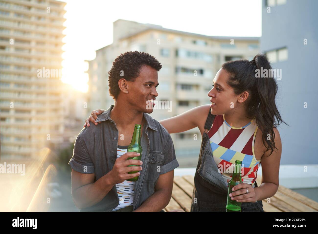 Happy young couple drinking beer on sunny urban rooftop balcony Stock Photo