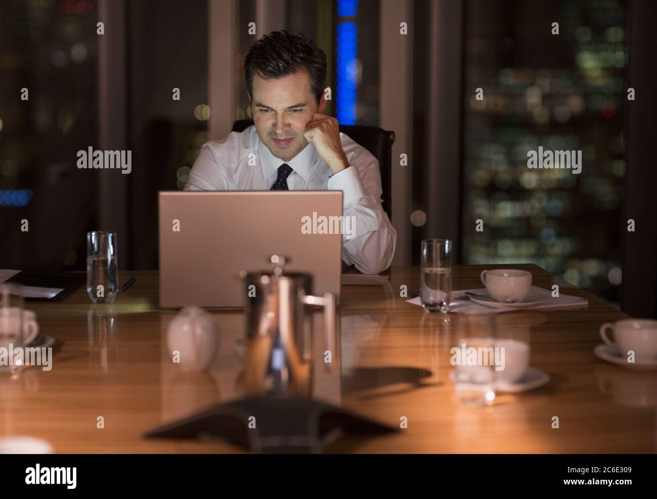 Businessman working late at laptop in conference room at night Stock Photo