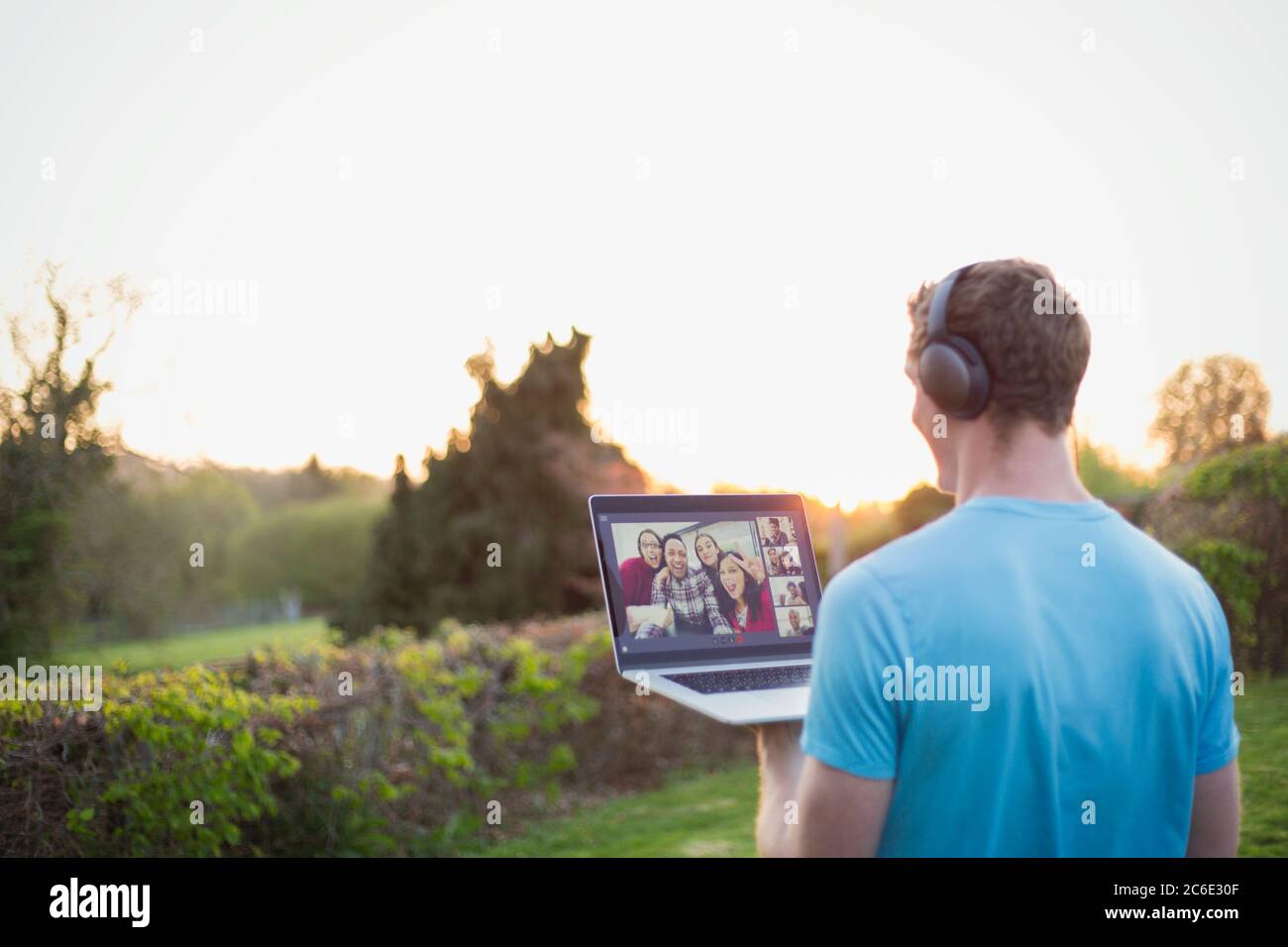 Man with headphones video chatting with friends in sunny garden Stock Photo