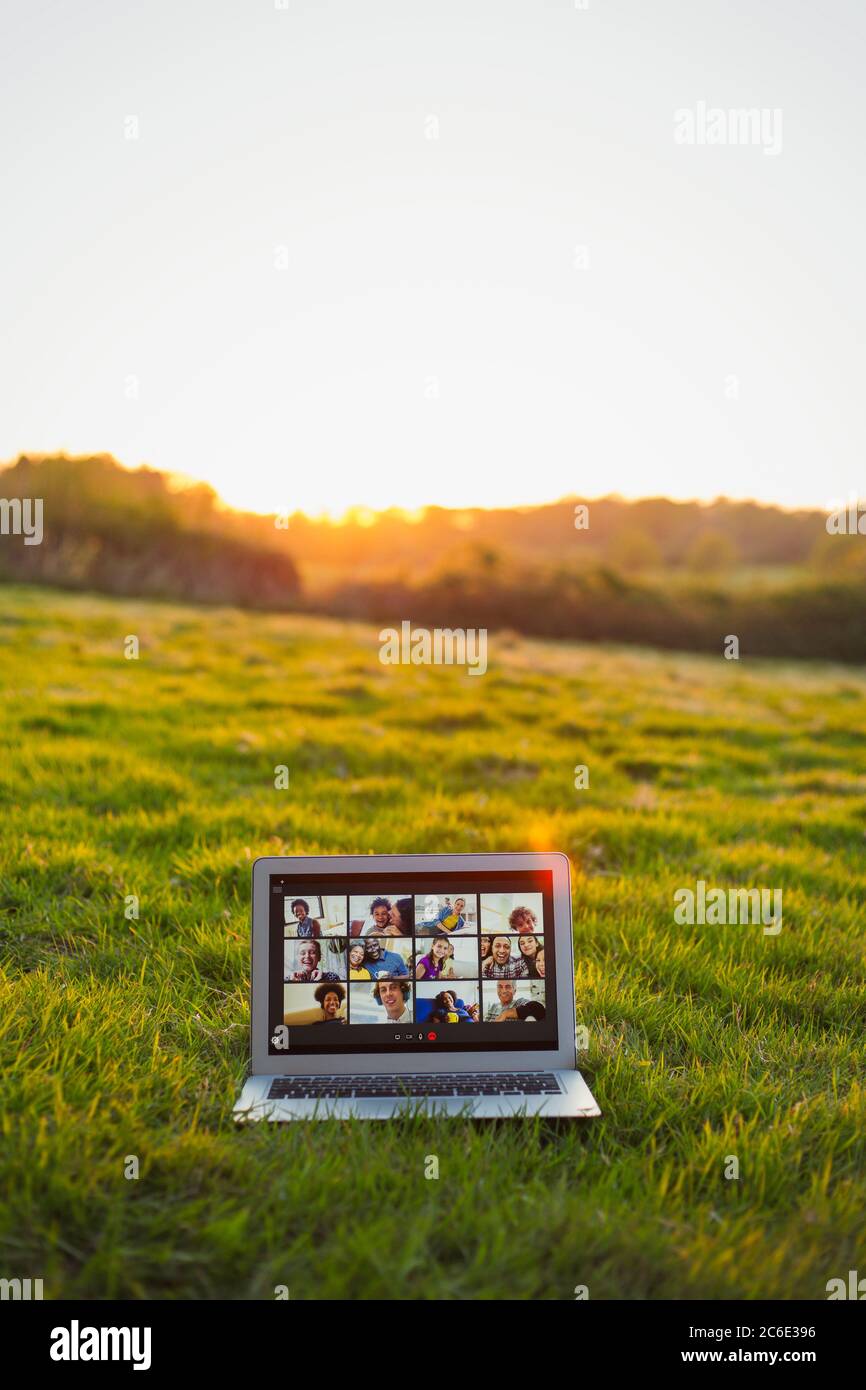 Friends video chatting on laptop screen in sunny grass field Stock Photo
