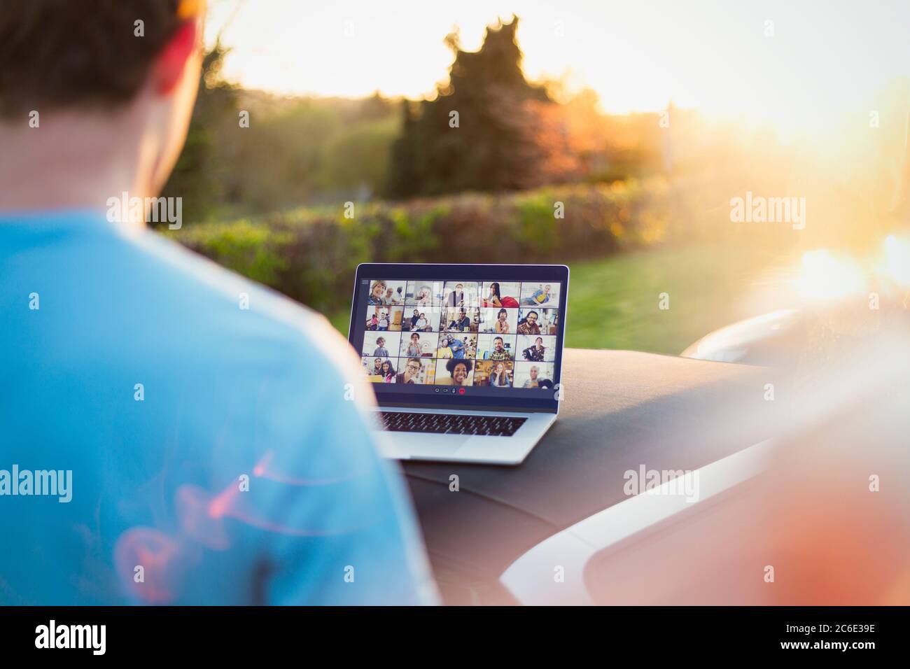 Man video chatting with friends on laptop screen on top of car Stock Photo