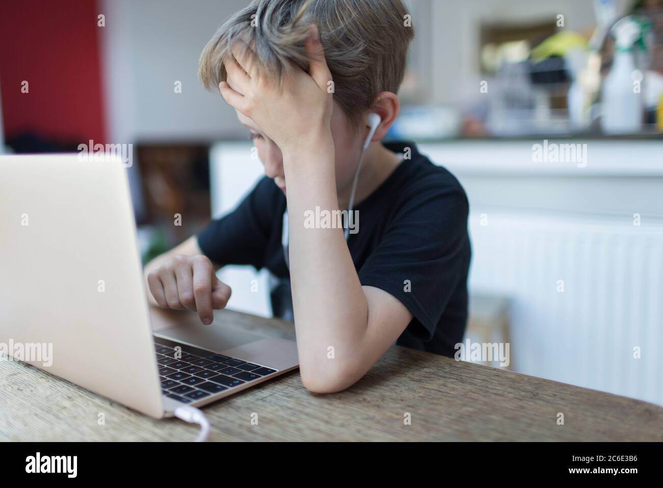 Frustrated boy with headphones homeschooling at laptop Stock Photo
