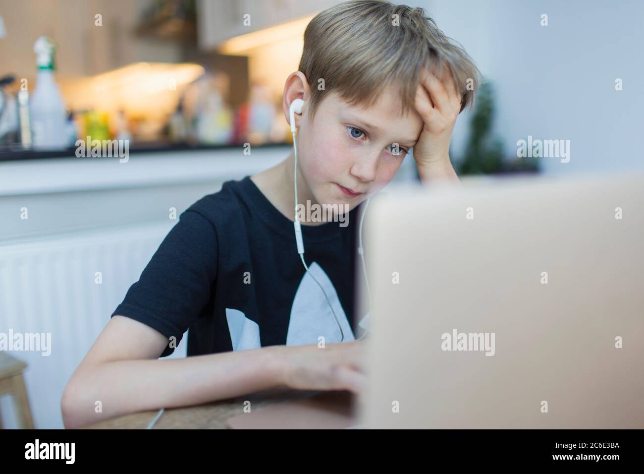 Focused boy with headphones using laptop in kitchen Stock Photo