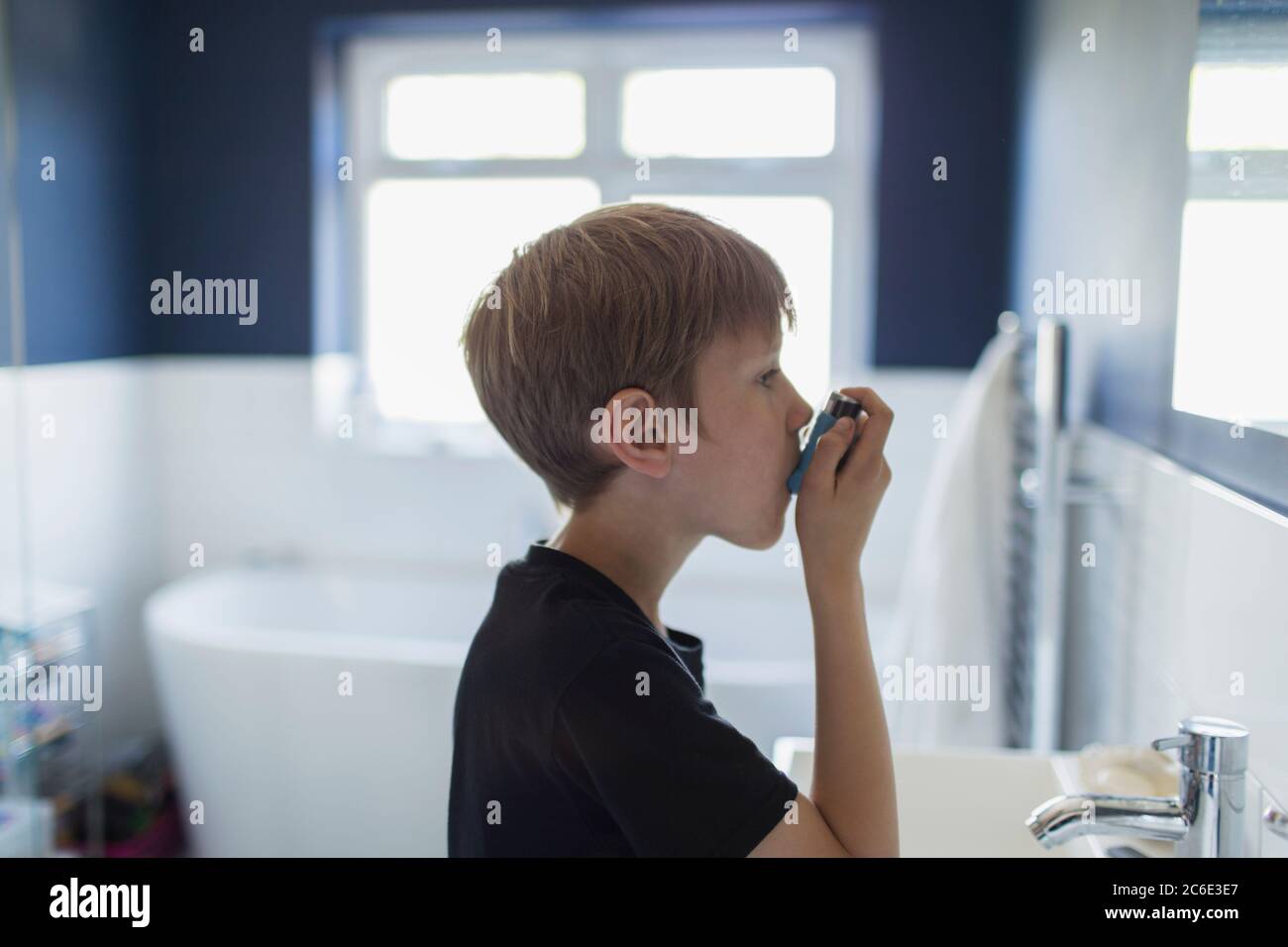 Boy with asthma using inhaler in bathroom Stock Photo