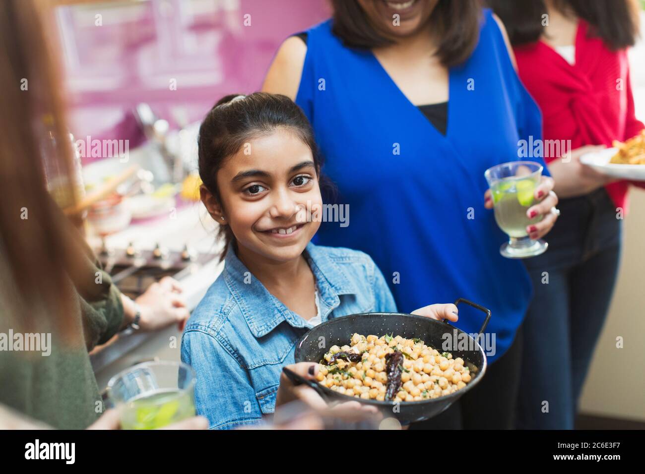 Portrait smiling Indian girl preparing food with family in kitchen Stock Photo
