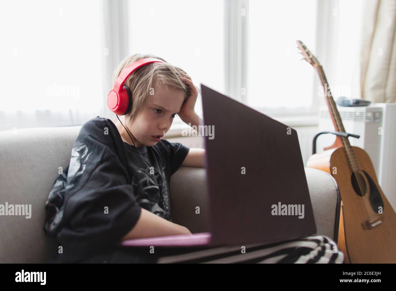 Boy with headphones and laptop on living room sofa Stock Photo