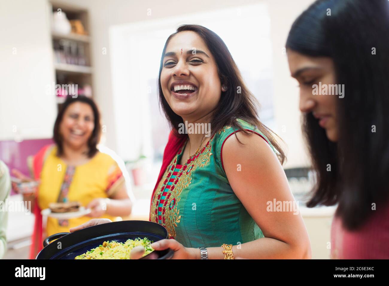 Happy Indian woman in sari preparing food with family in kitchen Stock Photo
