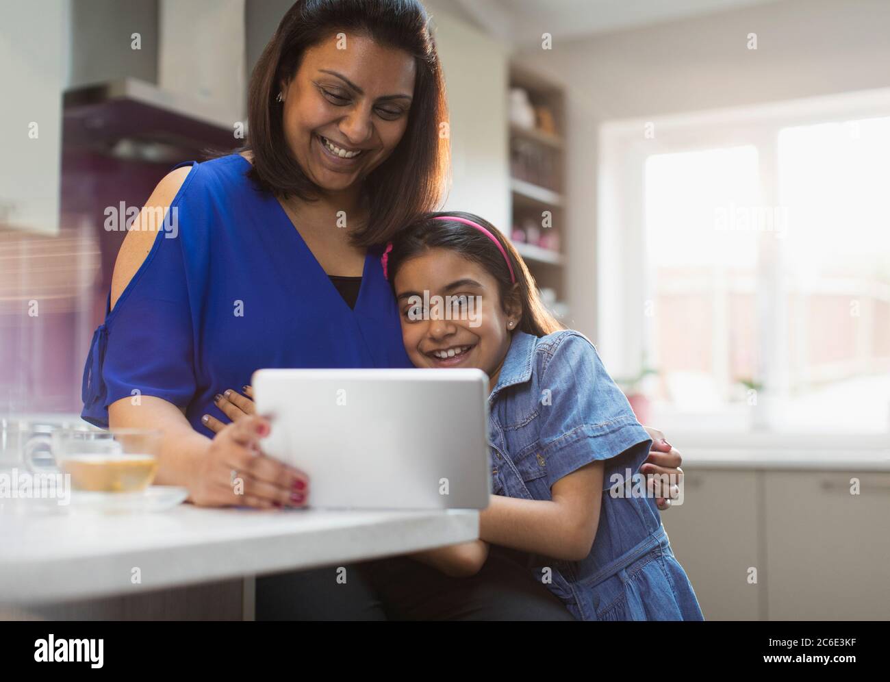 Smiling mother and daughter using digital tablet in kitchen Stock Photo