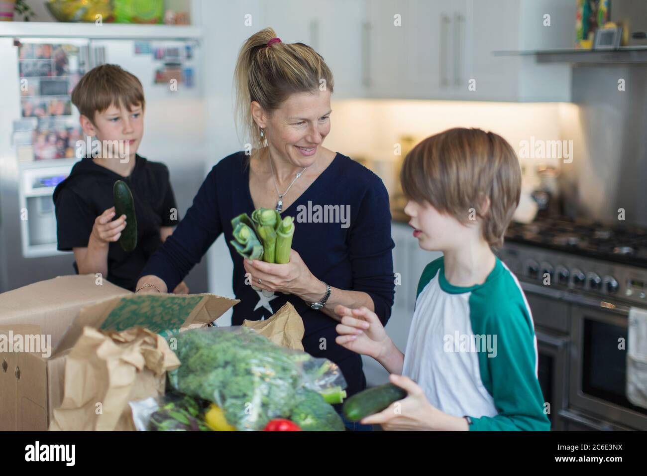 Happy mother and sons unloading fresh produce from box in kitchen Stock Photo