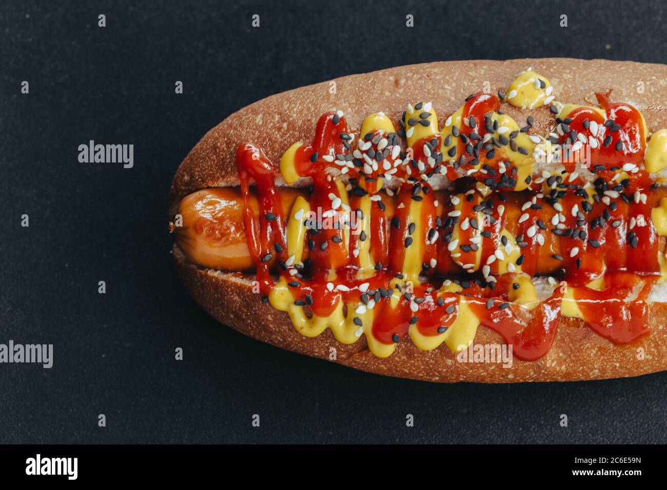 Gourmet dirty hot dog sandwich with various garnish on black slate