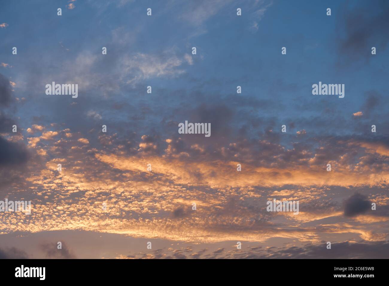 Setting or rising sun tinting Stratocumulus Cumulus as dramatic layers of clouds reflecting different sun rays due to altitude Stock Photo