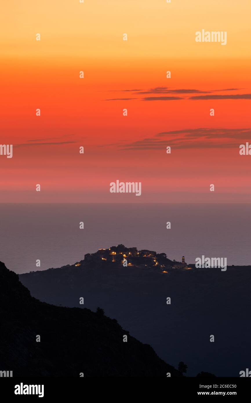 Orange afterglow after the sun has set over the Mediterrnean sea with the silhouetted hilltop village of Sant'Antonino in Corsica in the foreground Stock Photo