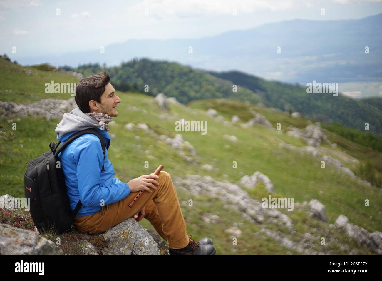 A young male tourist on the summit of Stara Planina (Balkan Mountains) and enjoying the view. In one of his hands, he's holding a wooden reed-pipe. Stock Photo