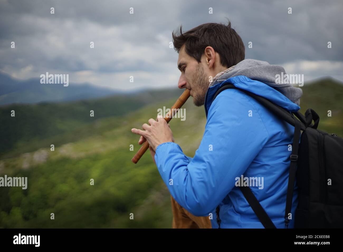 A side view of a young male tourist playing a wooden reed-pipe/ flute. He is on the summit of Stara Planina (Balkan Mountains). Stock Photo