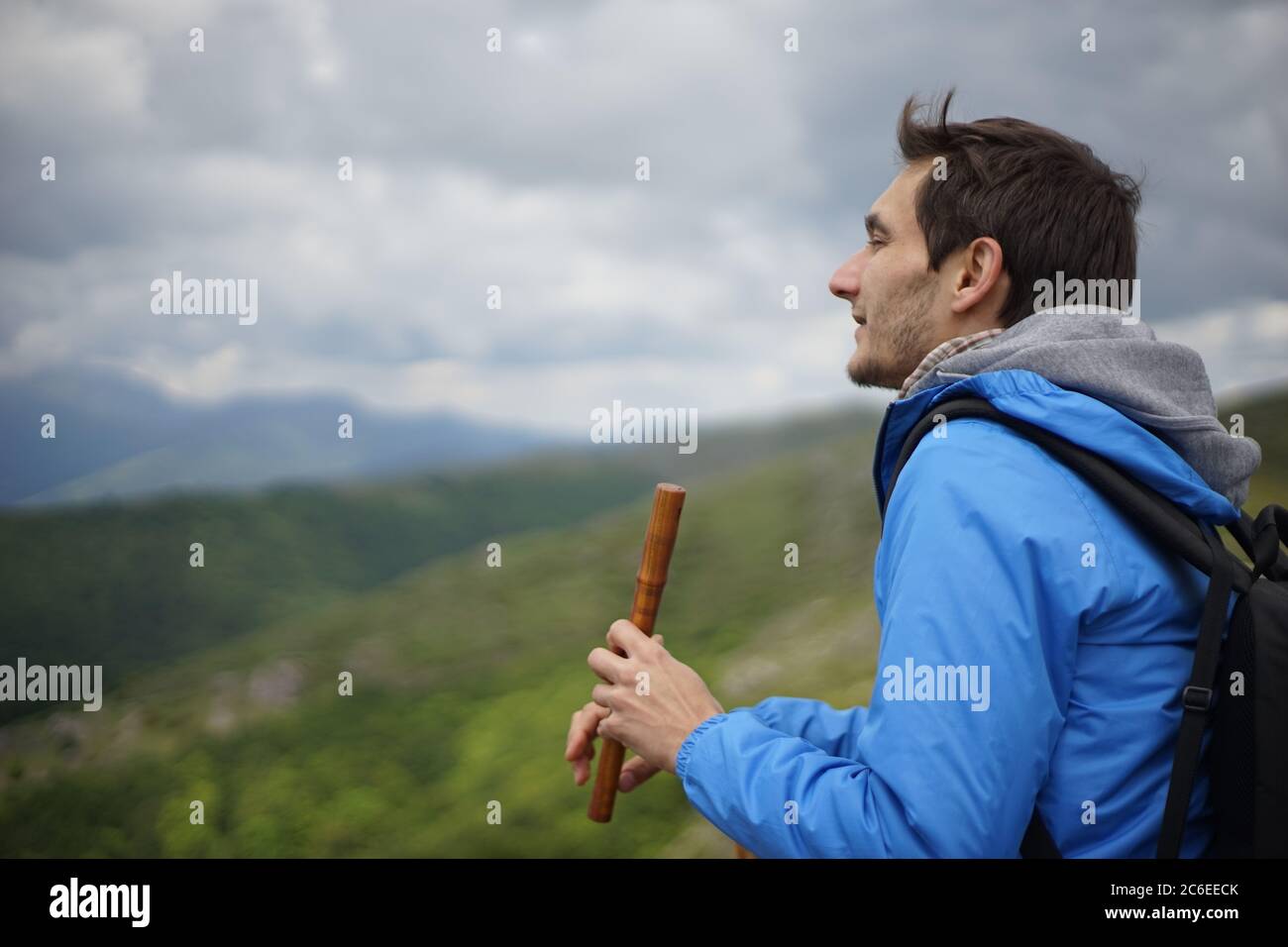 A side view of a young male tourist playing a wooden reed-pipe/ flute. He is on the summit of Stara Planina (Balkan Mountains). Stock Photo