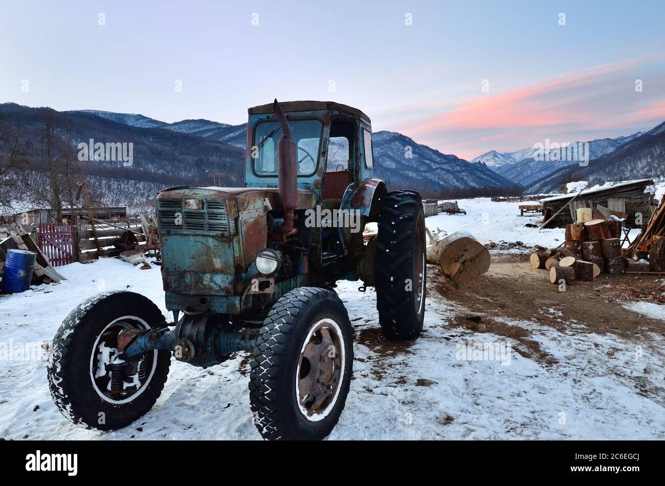 Caucasus, Russia - Feb 18, 2012: Old rusty soviet tractor shown on courtyard farmhouse in village in mountain region of Caucasus mountain at sunrise i Stock Photo