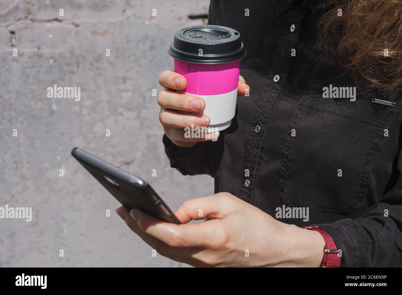 Girl with coffee cup holds smartphone in hand close-up Stock Photo