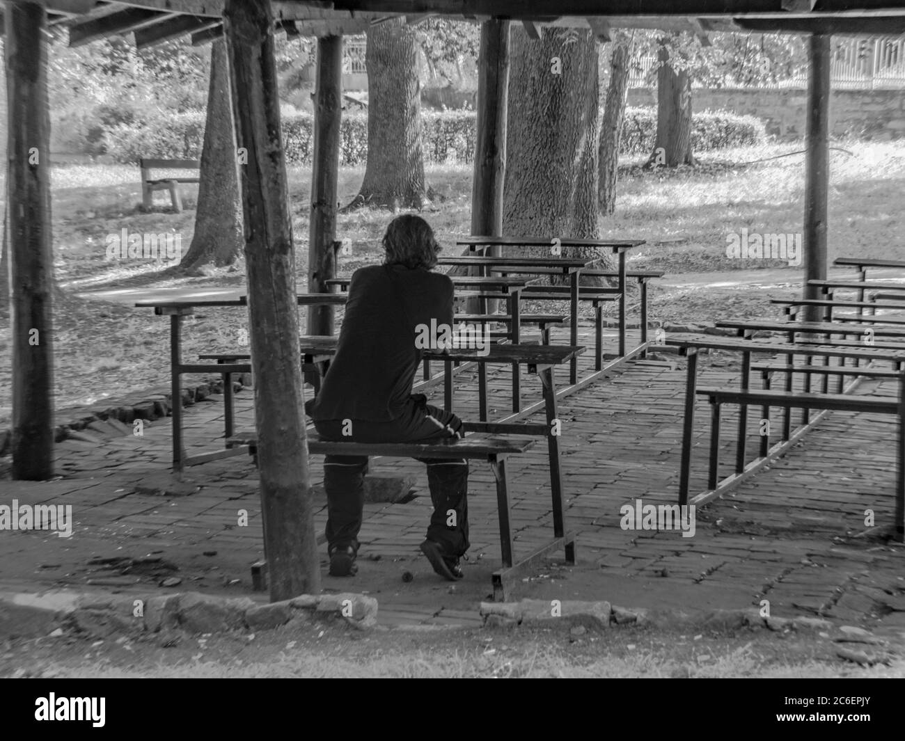 Teacher sitting in empty outdoor classroom alone in nature, monochrome Stock Photo