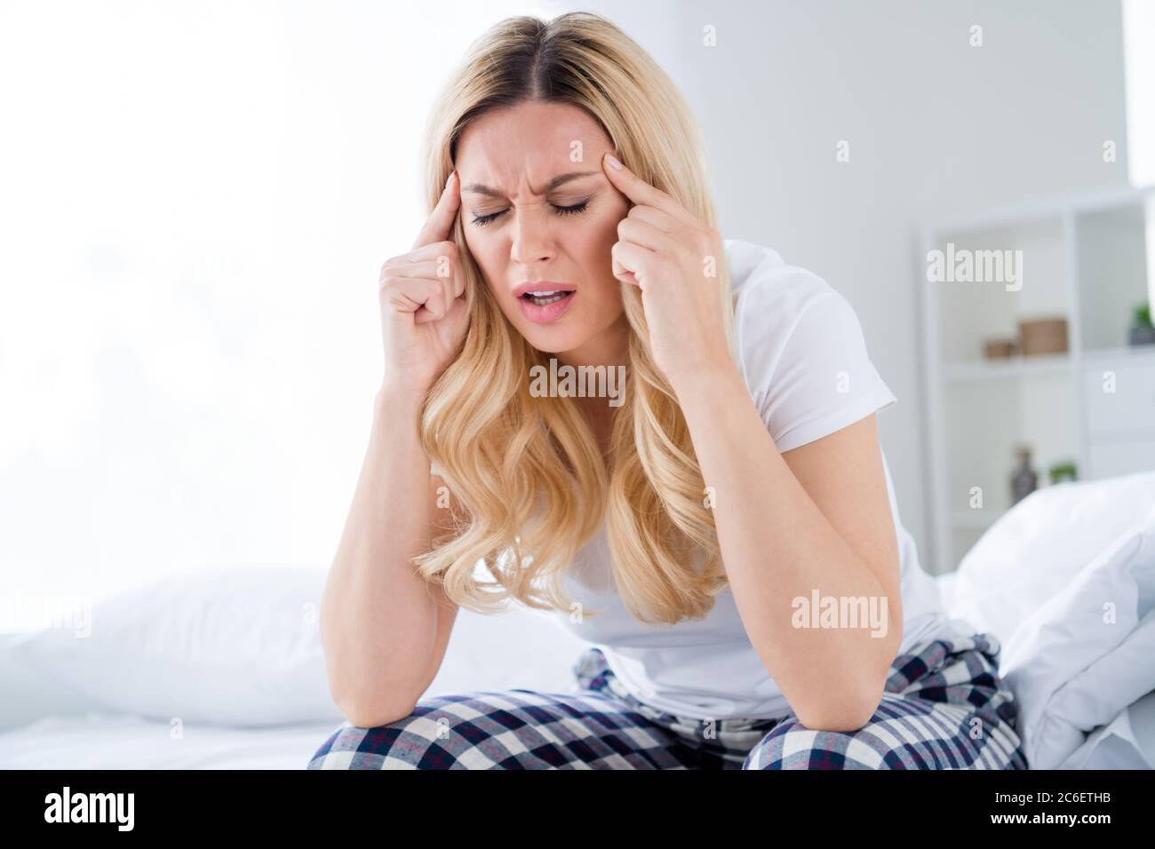 Photo of displeased blond house wife lady sitting bed white sheets quarantine time stay home suffer morning terrible migraine hold touch fingers Stock Photo