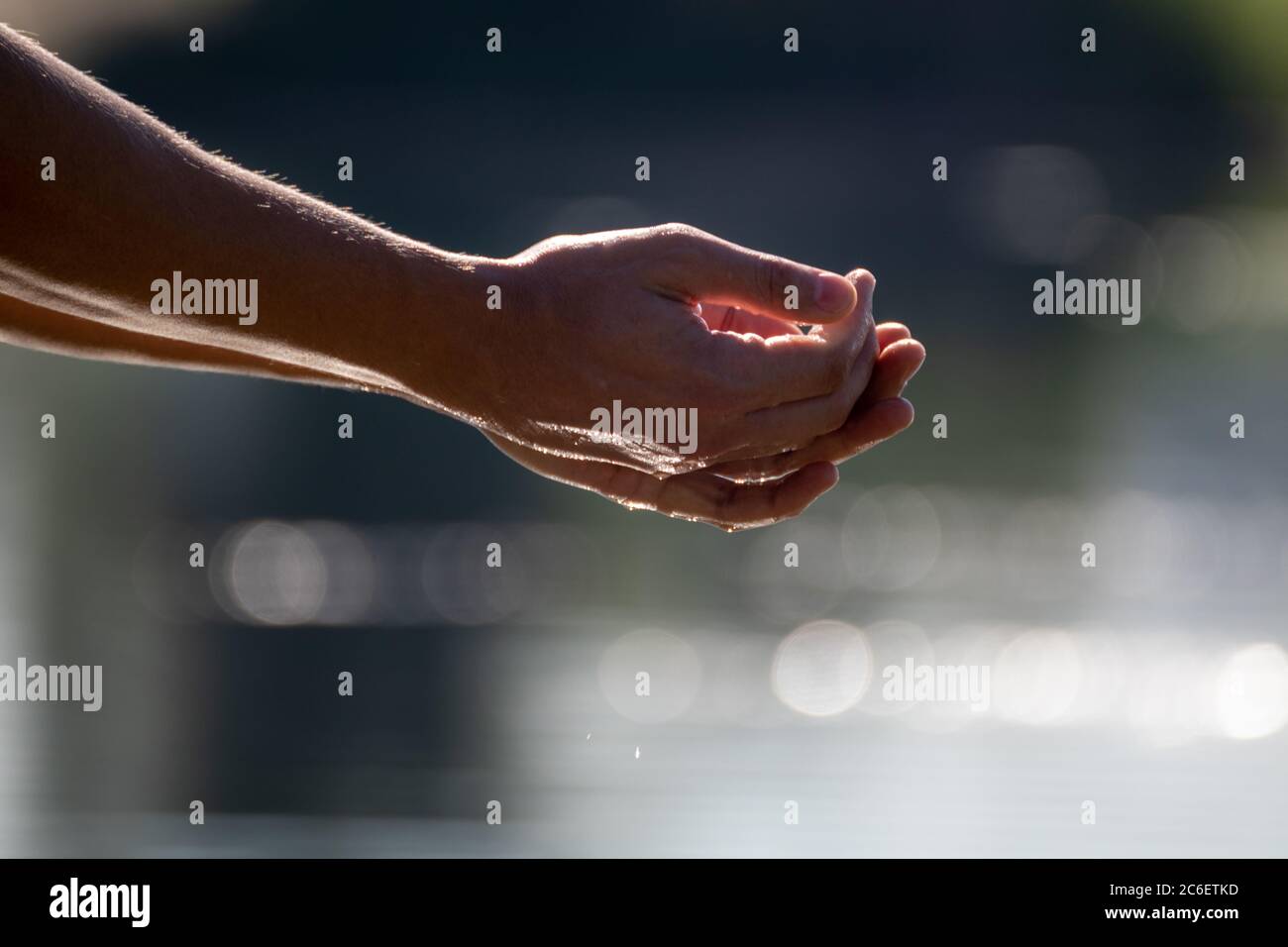 Close-up shot of hands cupping sea river water. Blue blurred water on bright sun beam. Slowly drops dropping into the water Stock Photo