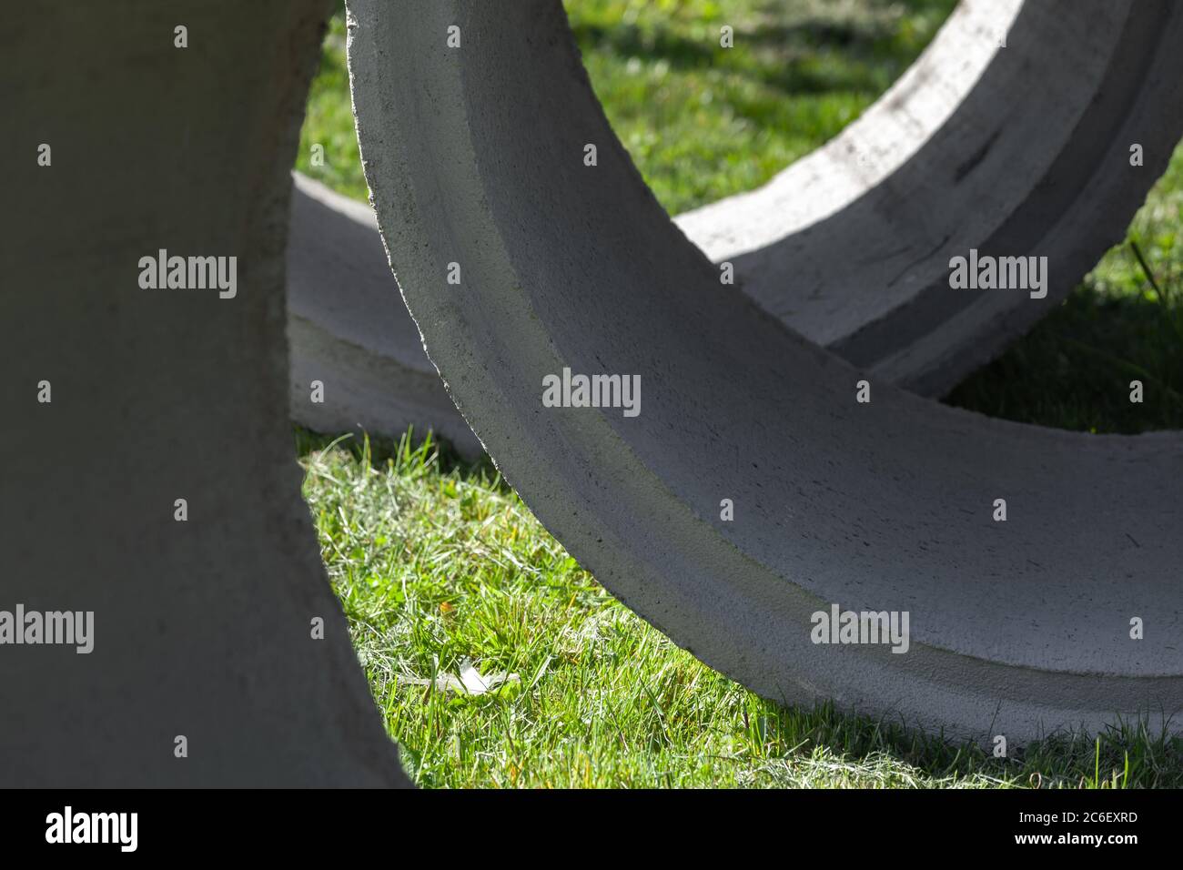 Massive concrete rings lay on green grass, abstract industrial photo background Stock Photo