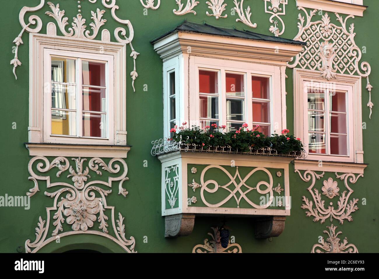 Facade of a beautiful green baroque house in Scharding, Austria featuring a small oriel window decorated with pink geranium flowers. Stock Photo