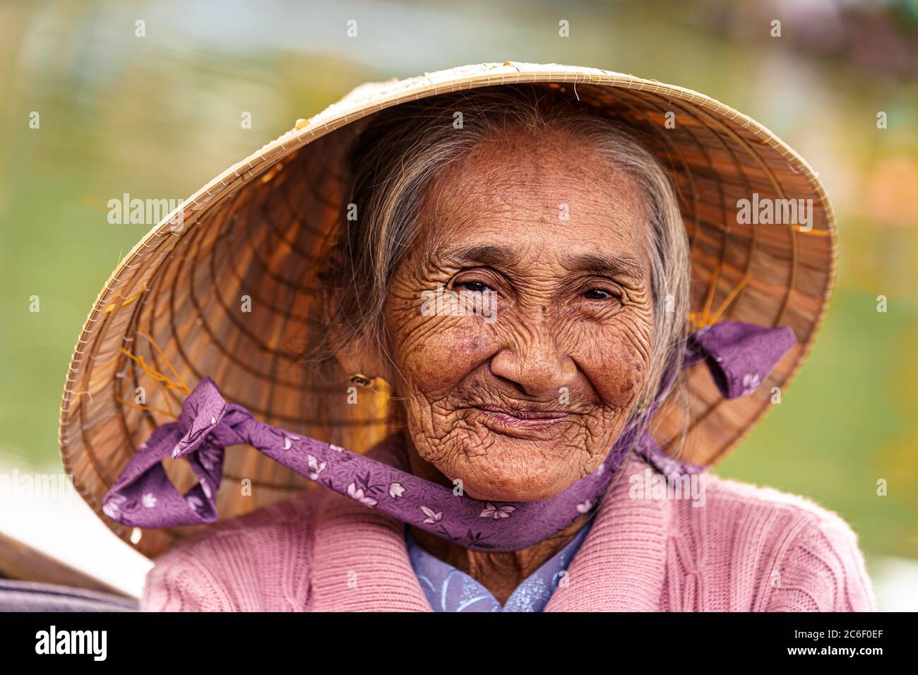 Vietnamese old woman in violet sweater and hat smiles at camera Stock Photo