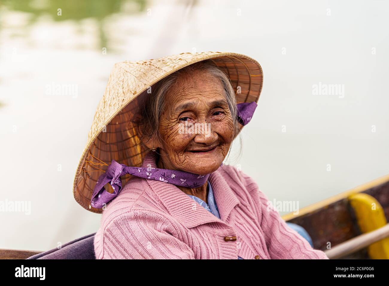 Vietnamese old woman in violet sweater and hat is sitting on a boat while smiling Stock Photo