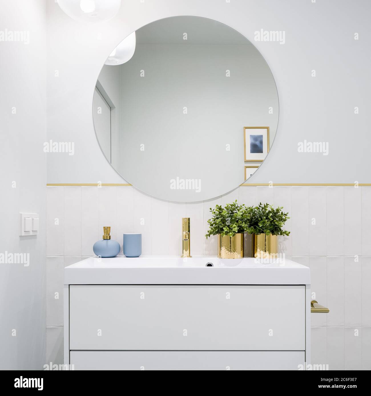 Bright bathroom with round mirror, white cabinet with drawers and blue and golden decorations Stock Photo