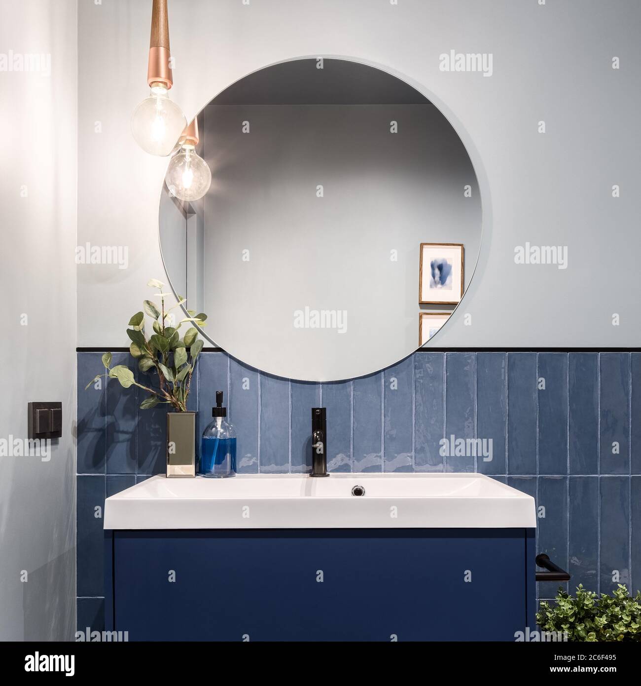 Designed bathroom with stylish blue cabinet, blue wall tiles and big round mirror Stock Photo