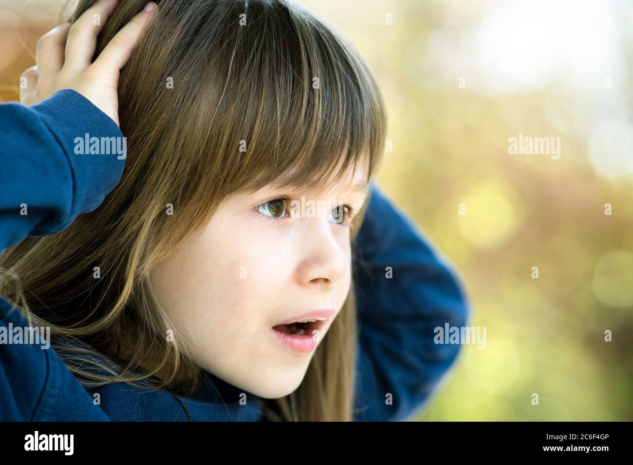 Portrait of surprised child girl holding hands to her head outdoors in ...