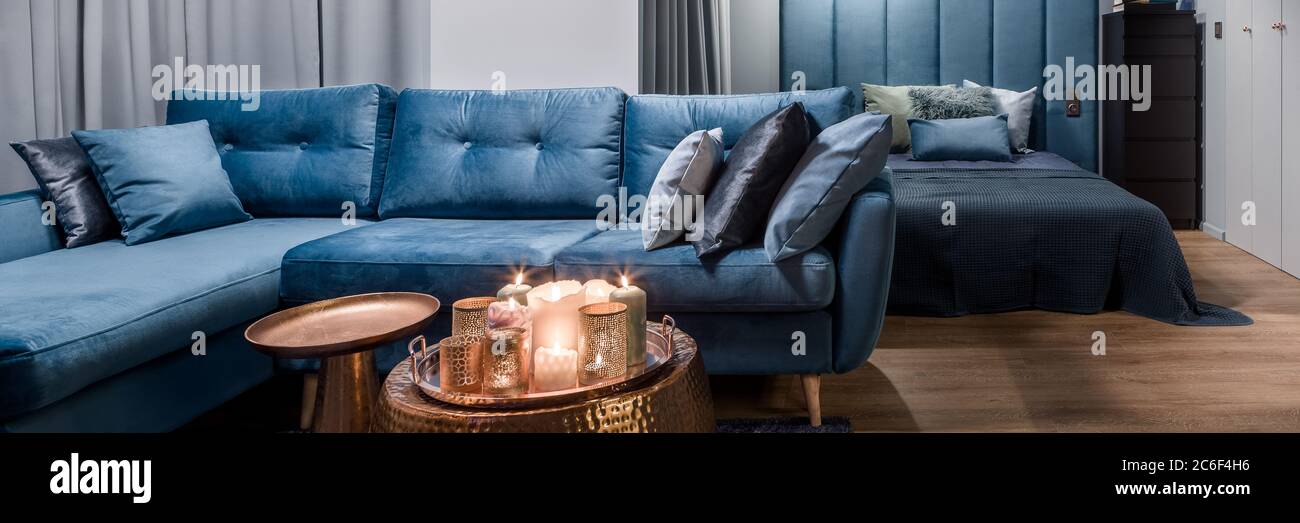 Panorama of apartment in blue with big corner sofa, copper coffee tables with decorations and open bedroom Stock Photo