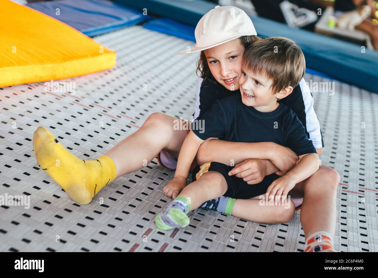 Funny smiling kids on trampoline. Older brother embraces younger