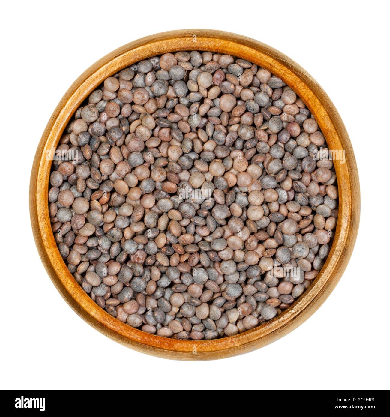 Unpeeled red lentils in wooden bowl. Dried seeds of Lens culinaris with their hulls, an edible legume, staple and a food crop. Closeup, from above. Stock Photo