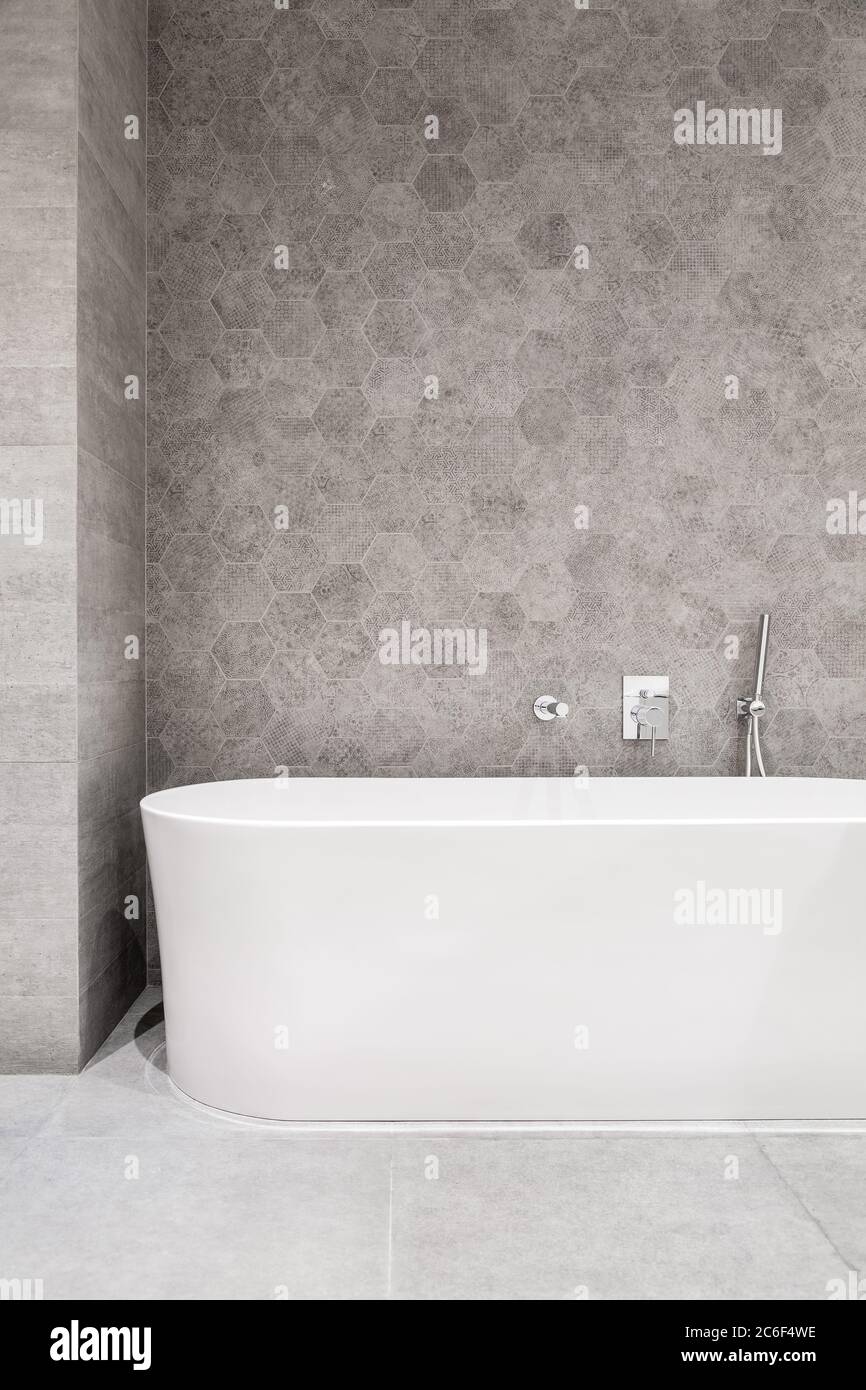 Modern bathroom with white bathtub and gray, hexagonal wall tiles Stock Photo