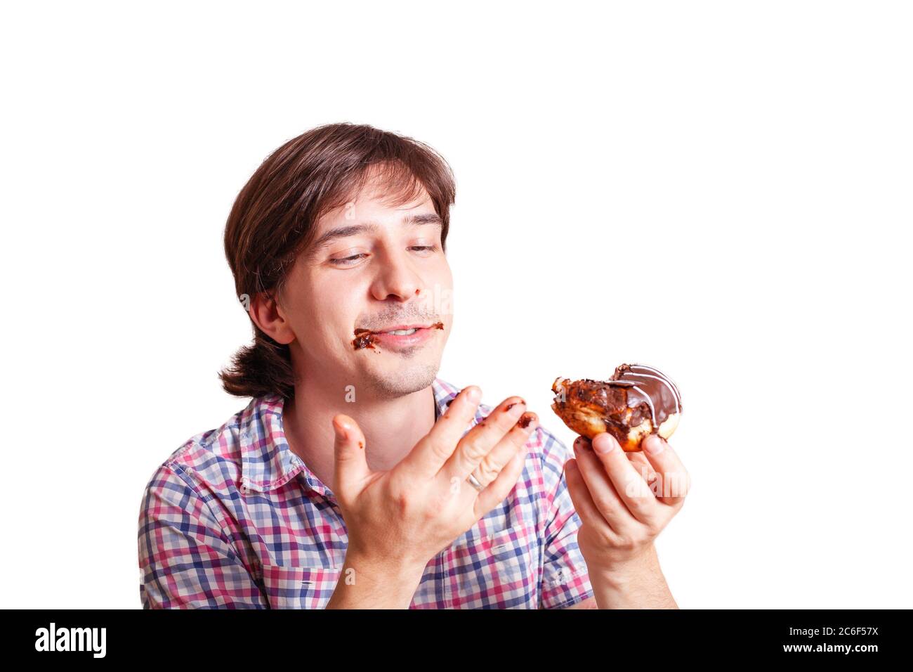 A man eats a doughnut and licks, a very funny photo on a white background. Empty space for text. A man loves sweets chocolate. World Chocolate Day sto Stock Photo