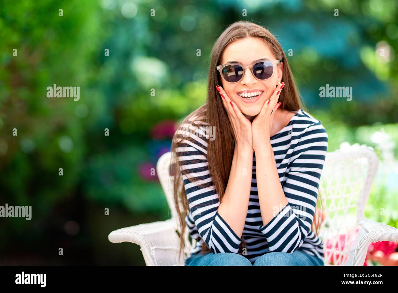 Portrait of an attractive mid 20’s woman gently touching her face while looking at camera and smiling outdoor. Happy woman relaxing in the garden at h Stock Photo