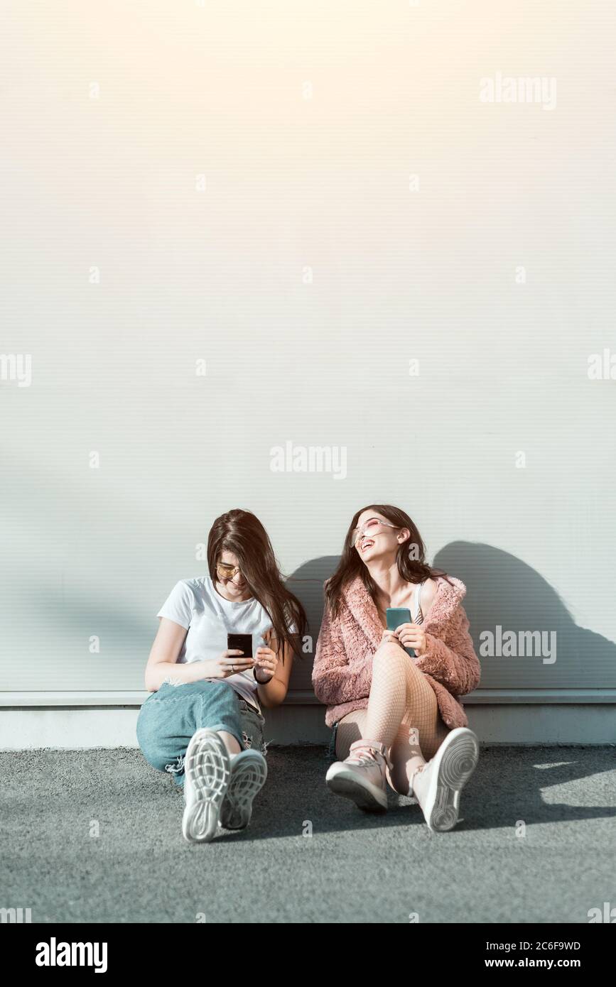 Two young female friends using mobile phones and laughing Stock Photo