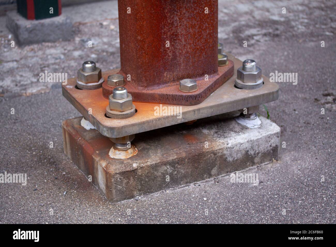 Anchoring of a rusty iron pillar to old concrete foundation with huge steel nuts and bolts