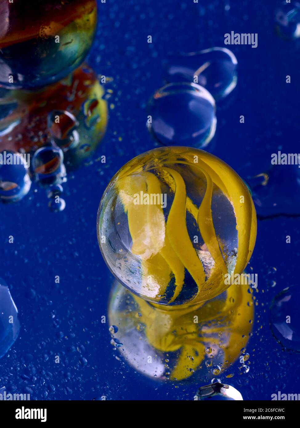 Blue accent colour, single glass marble and water droplets on blue