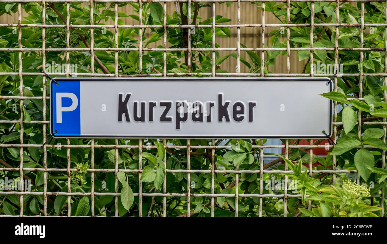 short term parking sign attached to a rusty fence in front of green shrubs, kurzparker in german language Stock Photo