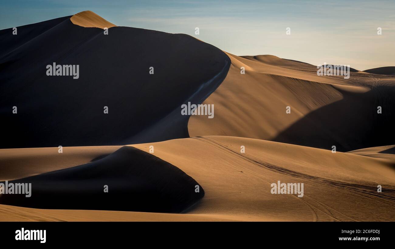 Path along stunning beige dunes outside in the desert with soft sunlight throwing shadows in the peaceful dusk. Stock Photo