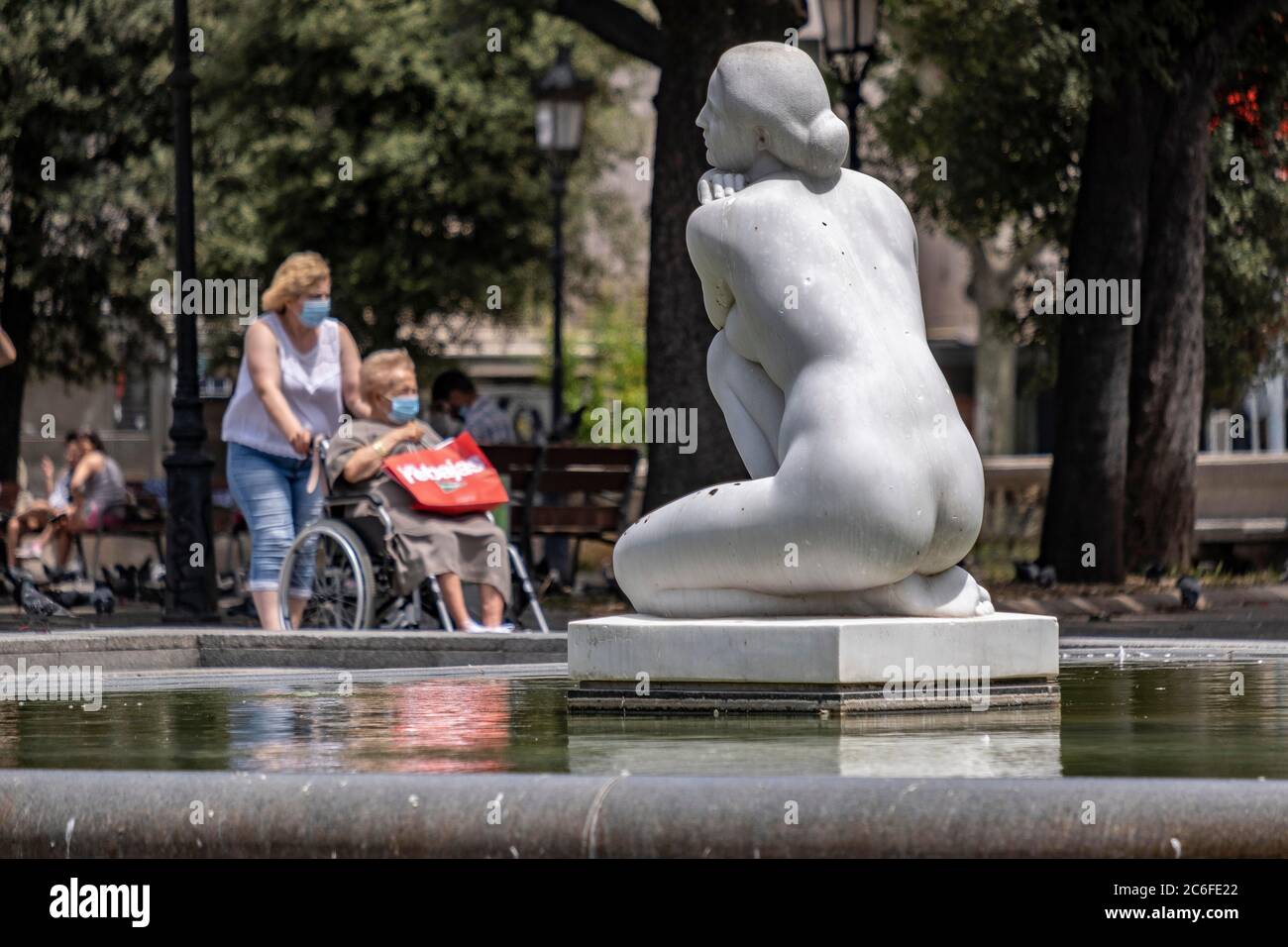Barcelona, Catalonia, Spain. 9th July, 2020. Two people seen next to the sculpture La Diosa by the sculptor Josep ClarÃ i Ayats in Plaza Catalunya while wearing face masks as a precaution against the spread of the coronavirus during the pandemic.Catalonia will fine whoever does not wear a sanitary mask in public space with 100 euros, as a measure due to the Covid-19 outbreak. Credit: Paco Freire/SOPA Images/ZUMA Wire/Alamy Live News Stock Photo