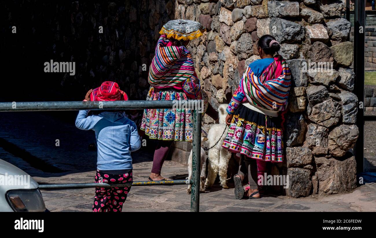 women in traditional colorful clothes in cusco peru in front of a stone wall. two women with alpaca, sheep and child Stock Photo
