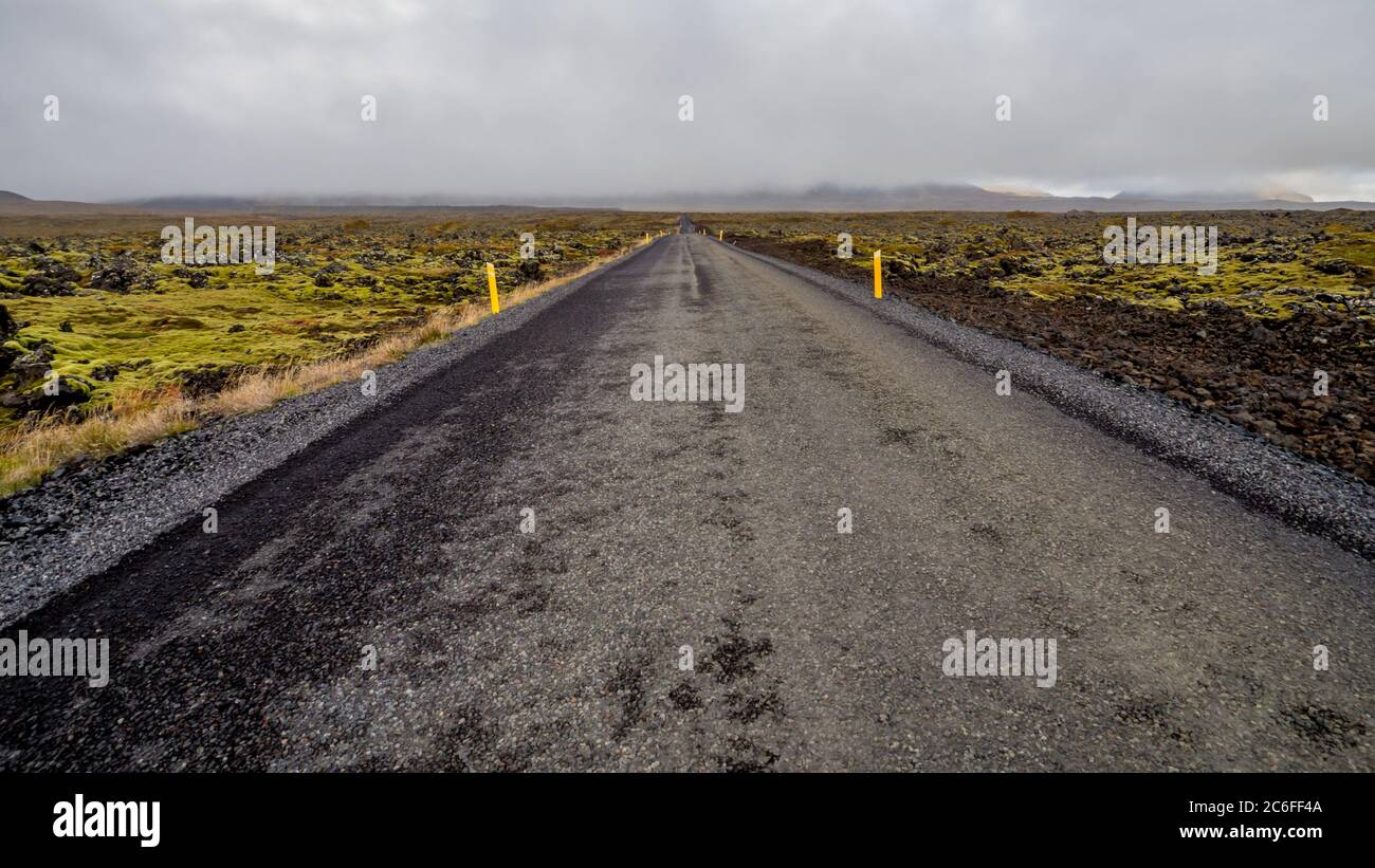 A straight empty asphalt roadway leads through endless lava fields overgrown with green moss at snaefellsnes peninsula in iceland Stock Photo