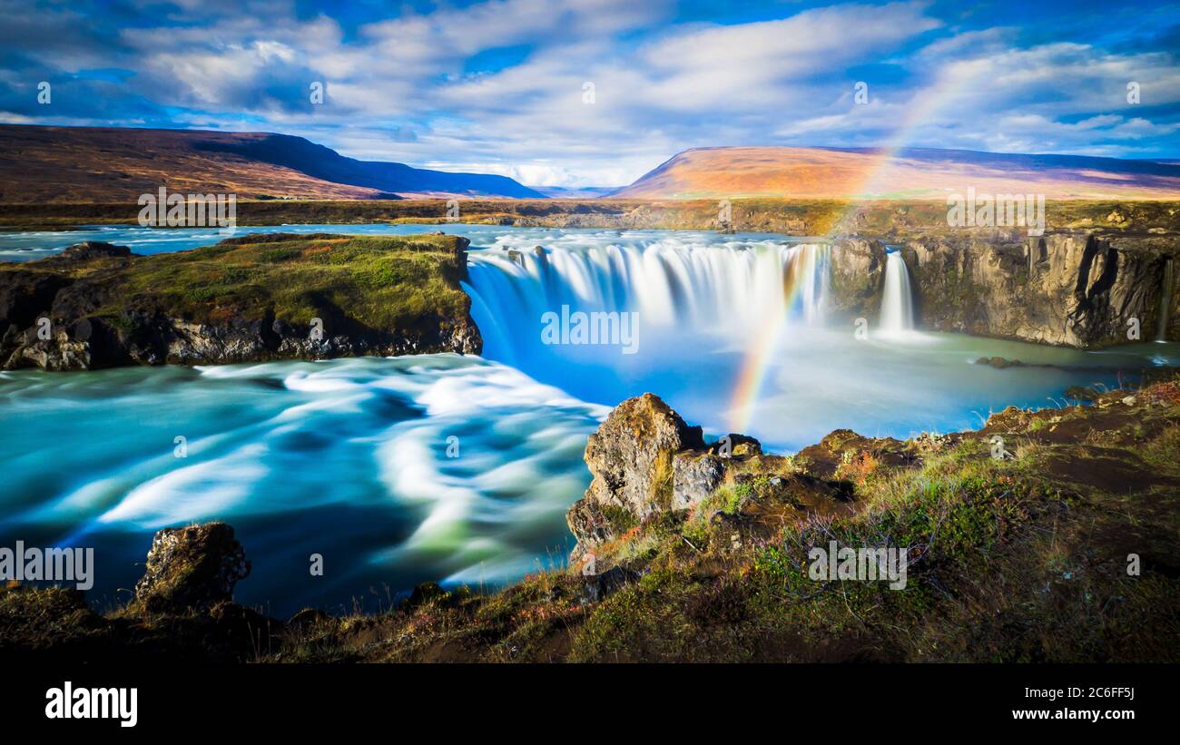 dynamic longtime exposure wide angle panorama of magical godafoss waterfall with romantic rainbow and hills in the background nearby fossholl, iceland Stock Photo